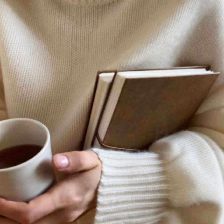 Woman holding books and a warm drink in a cosy knit jumper, the welcoming feel of a live wellbeing workshop