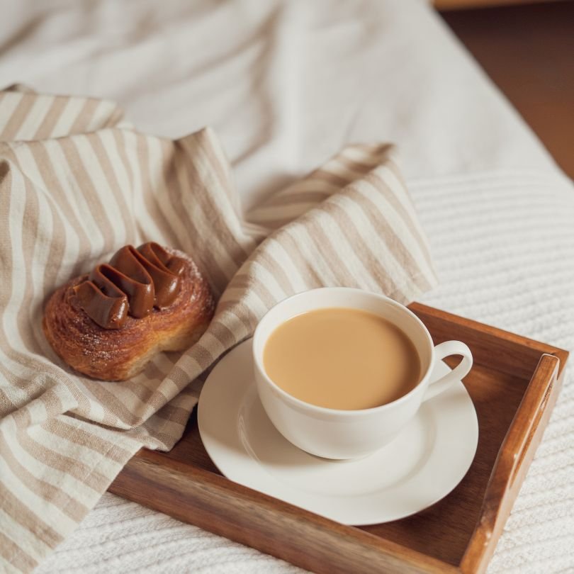 a cup of coffee and a pastry on a wooden tray, and a marble surface detail, evoking a calm and unhurried morning following hypnotherapy for sleep