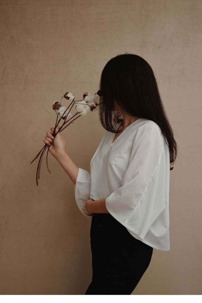 A woman in a white top holding dried flowers, looking away with a quiet, reflective expression