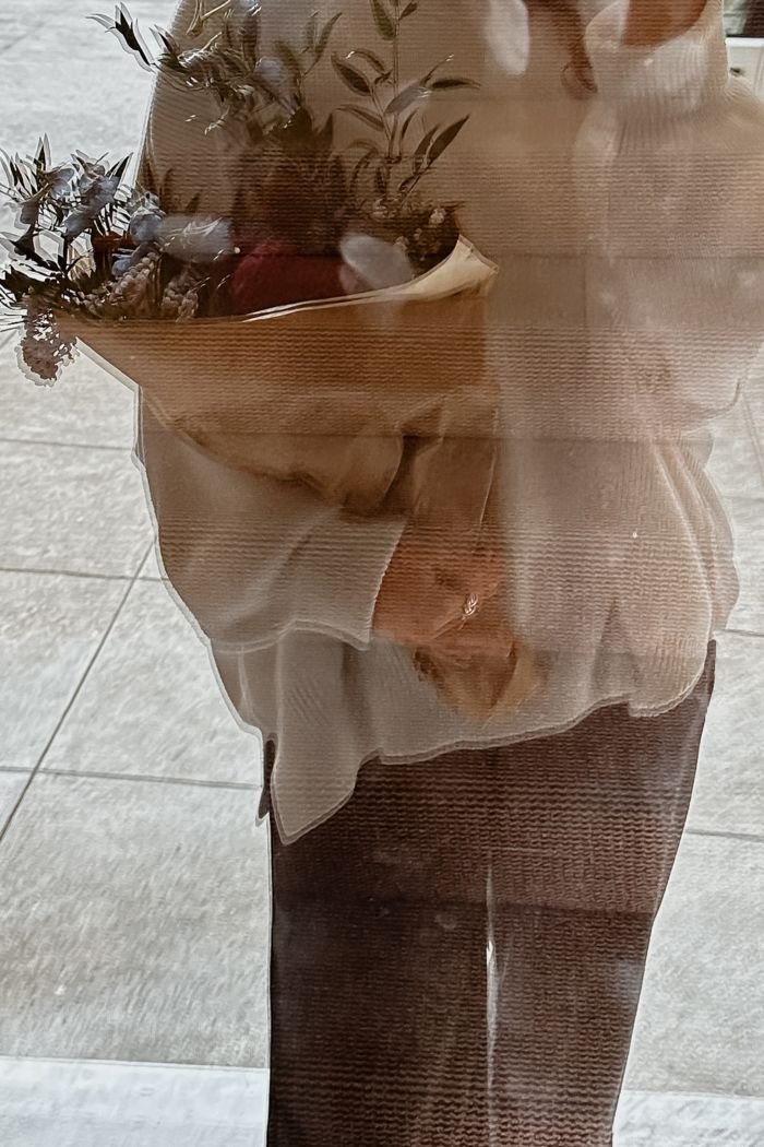 A woman's reflection in a window as she holds a bunch of flowers, a still and thoughtful moment feeling free from anxiety