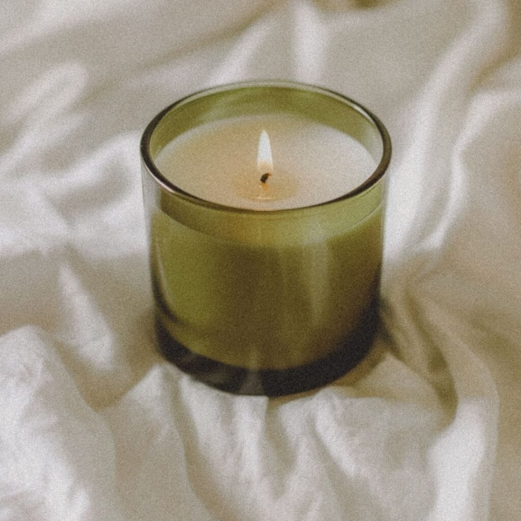 A green glass candle burning softly on white linen