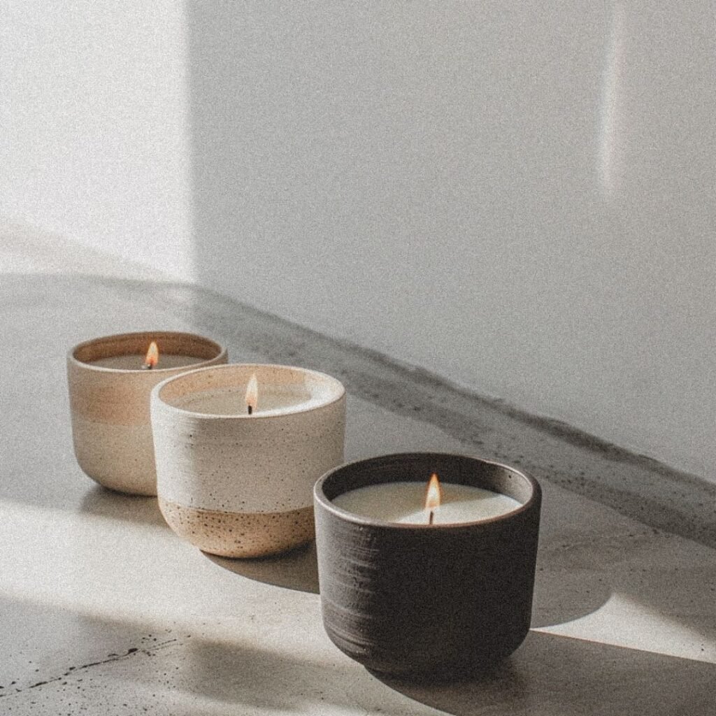 Three ceramic candles lit against a white wall in soft natural light, suggesting warmth and calm of hypnotherapy for anxiety