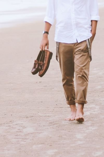 A person walking barefoot along a sandy beach, carrying shoes, evoking ease, freedom and a lighter way of moving through life
