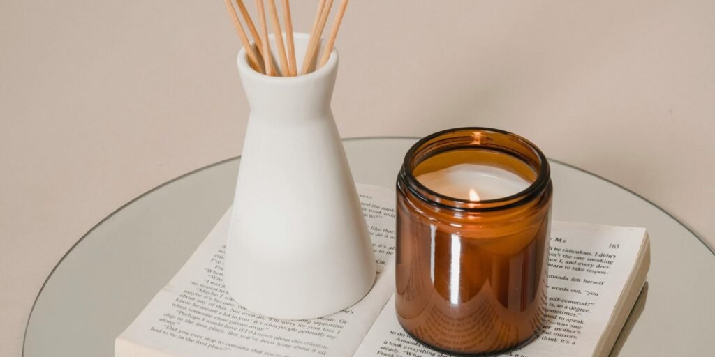 Reed diffuser in a white ceramic vase alongside an amber candle jar resting on a book, representing the calm and grounded atmosphere of between-session practice