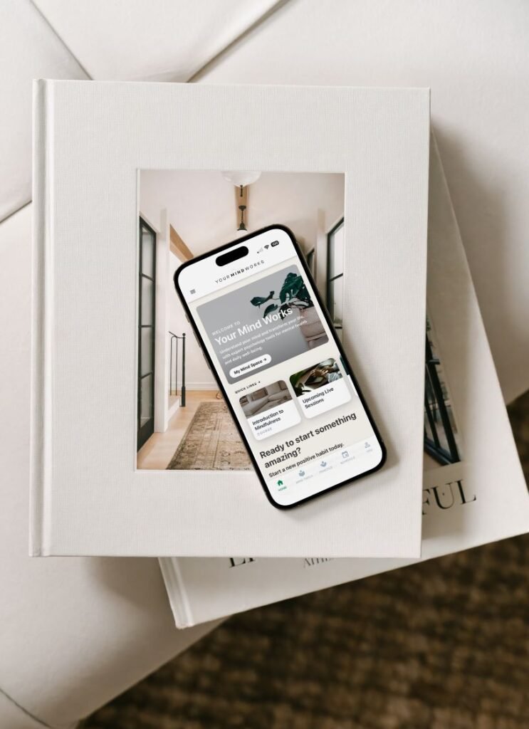 A mockup of the Your Mind Works app on top of a stack of wellbeing books
