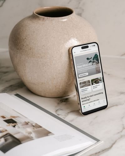our Mind Works app on a smartphone beside a ceramic vase, representing accessible wellbeing support between sessions