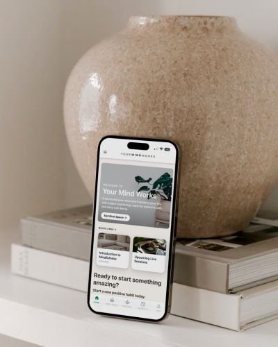 Your Mind Works app displayed on a phone screen, propped against a textured stone vase on a stack of books