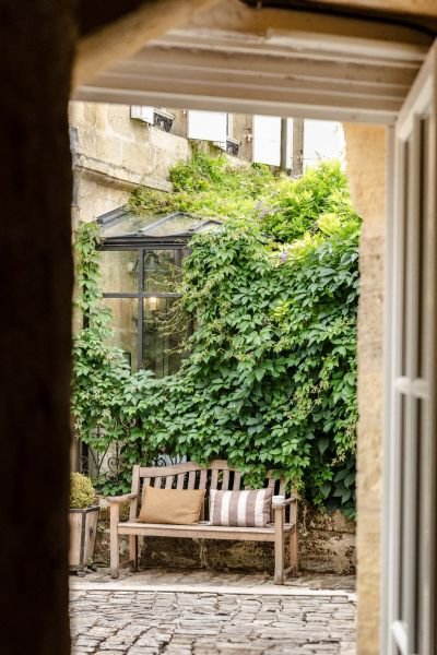 View through a doorway onto a sunlit cobblestone courtyard with wooden garden furniture and lush green foliage, representing the sense of openness and possibility that ACT therapy in Warwickshire is designed to develop