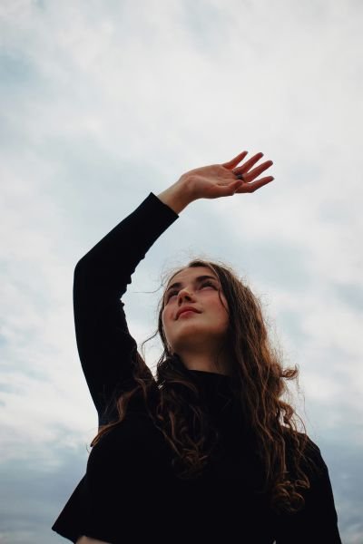 Woman reaching upward with arm raised against a cloudy sky, representing relief and a new perspective on stress
